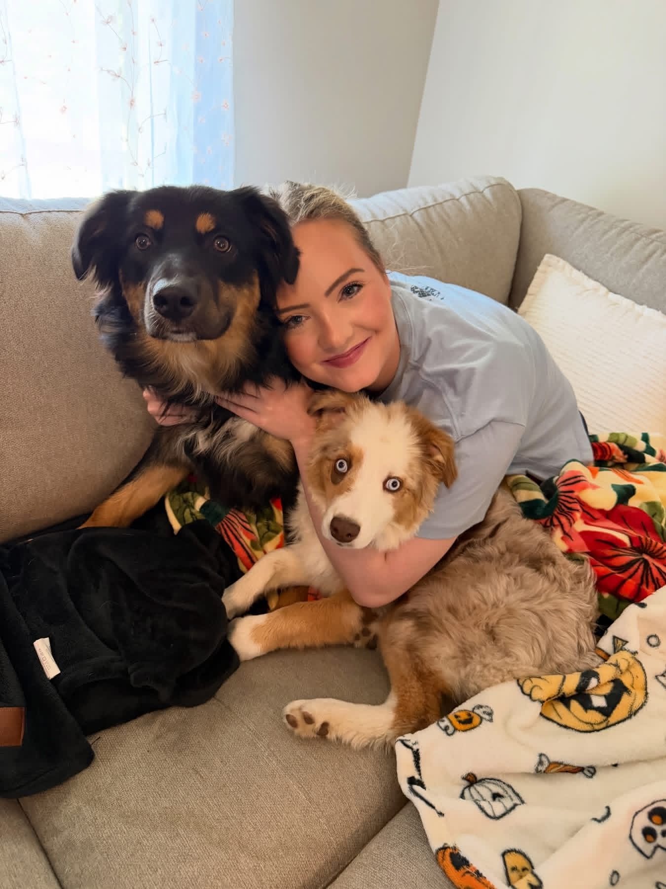 A woman cuddling two grown dogs on a couch