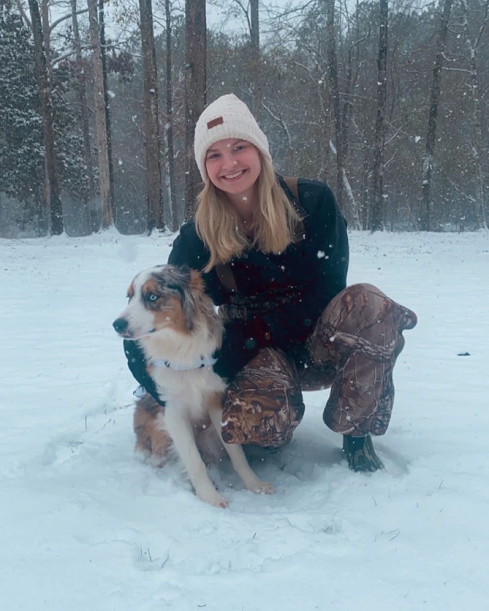 A woman crouching with her dog in the snow