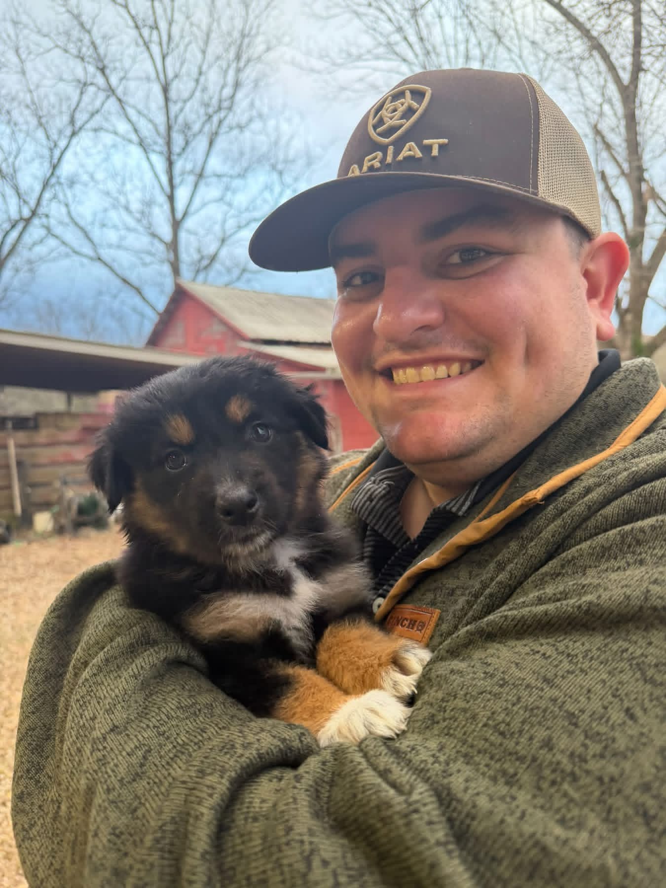A smiling man holding a black and tan puppy outdoors